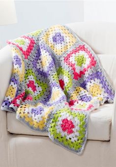 a crocheted granny blanket is sitting on a couch with a white chair in the background