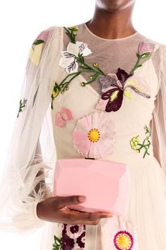 a woman in a white dress holding a pink box with flowers and butterflies on it