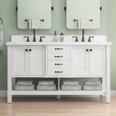 two white double sinks with mirrors above them in a green wall bathroom, one has folded towels on the floor