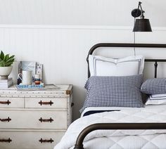 a bed with white and blue pillows on top of it next to two dressers