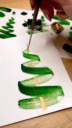 someone is painting cucumbers on paper with green paint and gold leaf decorations in the background