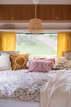 a bed with lots of pillows on top of it in front of a large window