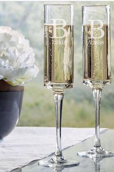 two champagne flutes sitting on top of a table next to a vase with white flowers