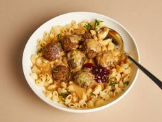 a white bowl filled with pasta and meatballs on top of a brown table next to a spoon