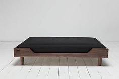 a wooden bed frame with black sheets on top and white walls in the back ground