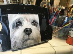 a painting of a white dog on a black box with colored pencils in the background