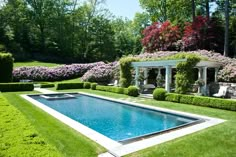 an outdoor swimming pool surrounded by lush green grass and bushes with trees in the background