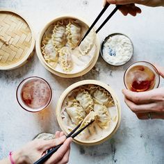 three people holding chopsticks and eating dumplings in bowls with drinks on the side