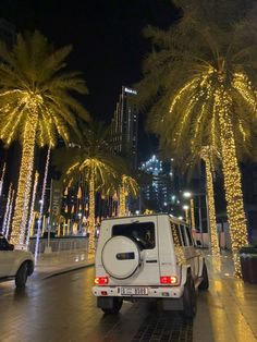 a white truck driving down a street next to palm trees covered in christmas lights at night