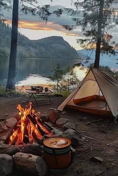 there is a tent and fire in the woods by the lake at sunset or sunrise