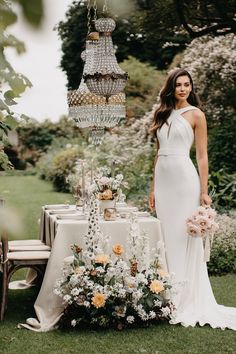 a woman standing next to a table with flowers and chandelier hanging from it