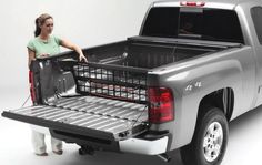 a woman standing next to the back of a silver pickup truck with its bed open