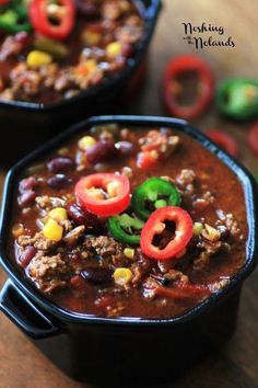 two black bowls filled with chili and ground beef stew on top of a wooden table