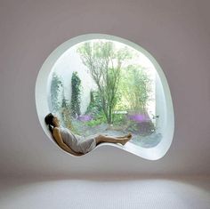 a woman laying on the floor in front of a round window with trees and bushes