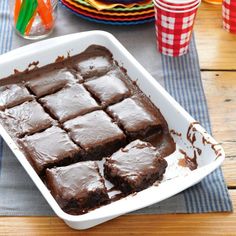 a white dish filled with brownies on top of a table next to plates and cups