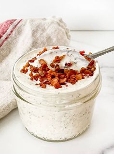 a glass jar filled with yogurt and bacon on top of a white counter