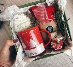 a red coffee mug sitting on top of a box filled with christmas decorations and gifts