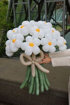 a bouquet of white flowers is being held by someone's hand with balloons attached to it