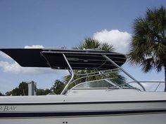 a white boat with a black cover on it's roof and palm trees in the background