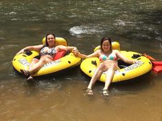 two women sitting on inflatable rafts floating down a river with their arms around each other