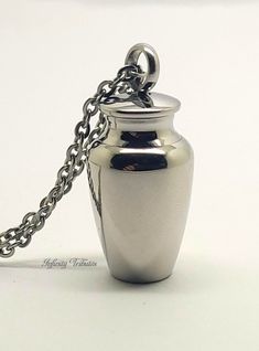 This stunning keepsake pendant/charm is made from premium-grade 316L non-tarnish stainless steel with a sleek and stylish urn design.  As with all of our keepsake jewellery, this piece incorporates a discreet chamber in which to hold a small, token amount of ashes, hair, fur, sacred earth or whatever you wish to hold close. This piece is also ideal for the safe transportation of a small quantity of pills/tablets (up to 8mm wide) All orders come complete with a presentation/gift box and a filling Ash Capsule Necklace, Sand Hair, Silver Amulet Necklace For Memorial, Urn Jewelry Spirit Piece Memorials, Urn Design, Sacred Earth, Urn Pendant, Urn Necklace, Keepsake Jewelry