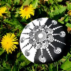 a black and white painted rock sitting in the grass with dandelions around it