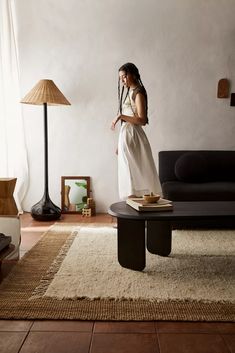 a woman standing in a living room next to a black couch and table with lamps on it