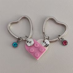 two heart shaped key chains with personalized charms on them, one is pink and the other is blue