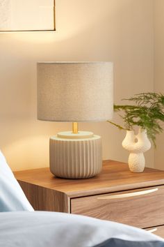 a white lamp sitting on top of a wooden table next to a night stand with a plant