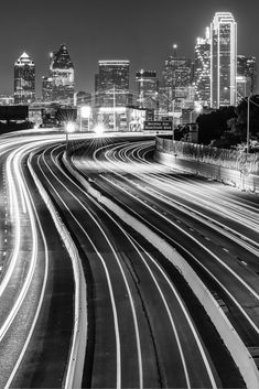 black and white photograph of city skyline at night with light trails in the foreground