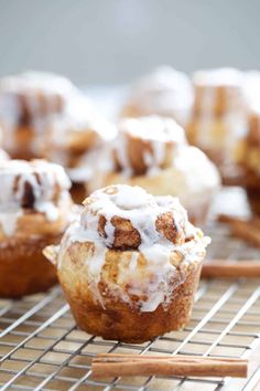 cinnamon roll muffins with icing and cinnamon sticks on a wire cooling rack