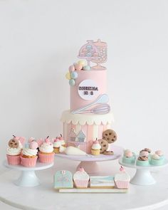 a pink and white cake with teddy bears on the top is surrounded by cupcakes