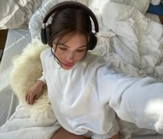 a woman laying in bed with headphones on her ears and looking down at the floor