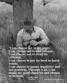 a man with a cowboy hat sitting in the grass next to a tree and holding a cat