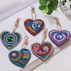 four heart shaped beaded key chains on top of a white table next to a plant