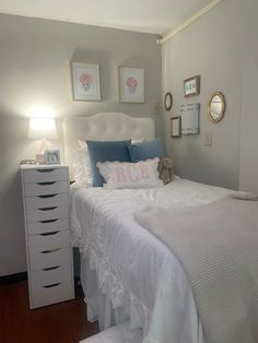 a white bed with blue and pink pillows on top of it next to a dresser