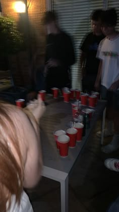 a group of people standing around a table with red cups on it and one person reaching for something