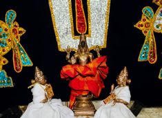 two statues are dressed in white and gold with colorful decorations on the wall behind them