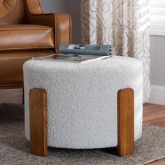 a white ottoman with wooden legs and a magazine on it's top, in front of a brown leather chair