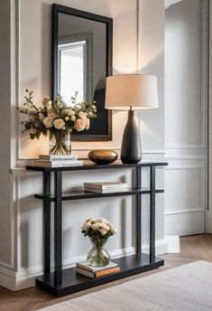 a black console table with flowers and a lamp on top in front of a mirror