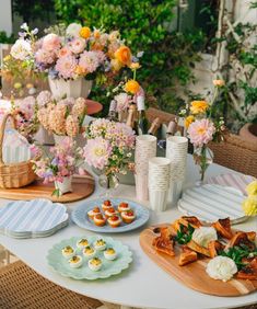 a table topped with plates and cups filled with food next to vases full of flowers