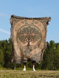 a person holding up a tapestry with a tree on it in the middle of a field