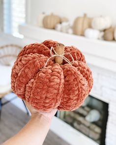 a person holding up a fake pumpkin in front of a fireplace