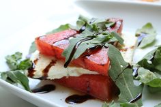 a white plate topped with slices of watermelon covered in sauce and leafy greens