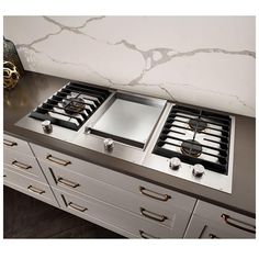 two burners on top of a stove in a kitchen with marble counter tops and drawers