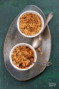 two bowls filled with granola sitting on top of a metal plate next to a spoon