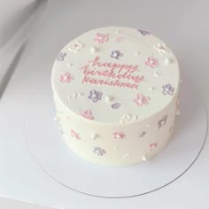 a white cake with pink and purple flowers on it's side sitting on a plate