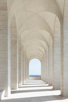 an empty walkway lined with white pillars leading to the ocean