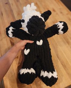 a hand is holding a black and white knitted stuffed animal on a wooden table