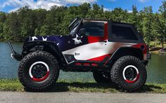 a red, white and blue jeep parked next to a lake